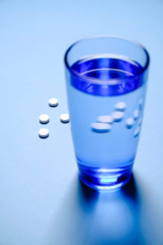 glass of water and white pills respresenting hydrocodone use