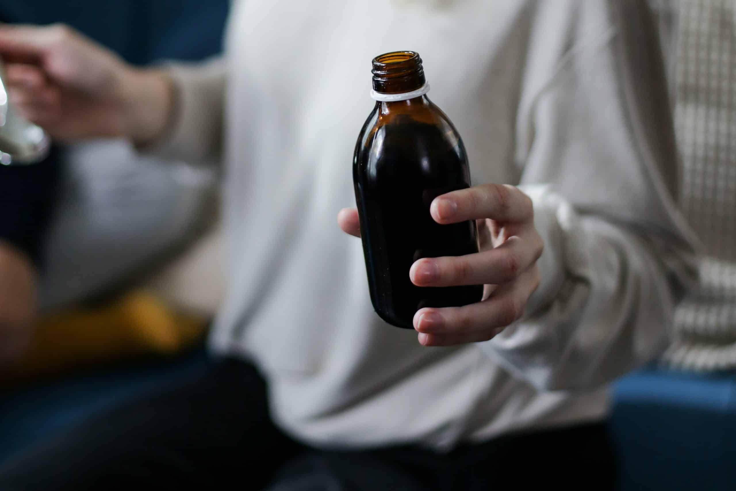 Person holding aa bottle of cough syrup and a spoon