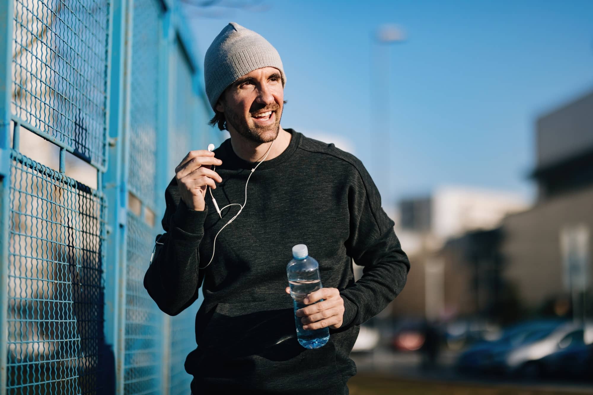 Happy male athlete with a bottle of water walking outdoors.