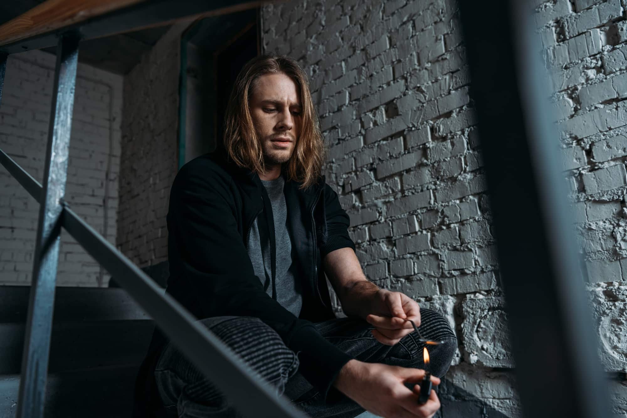 addicted man boiling heroin in spoon with lighter on stairs