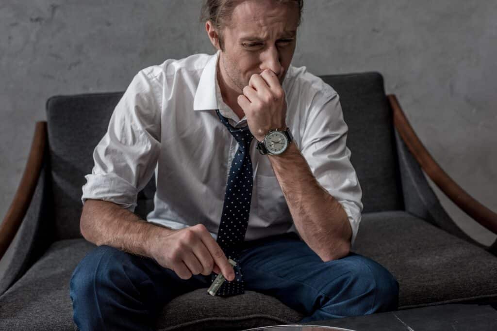 businessman with drug addiction sniffing cocaine while sitting on couch