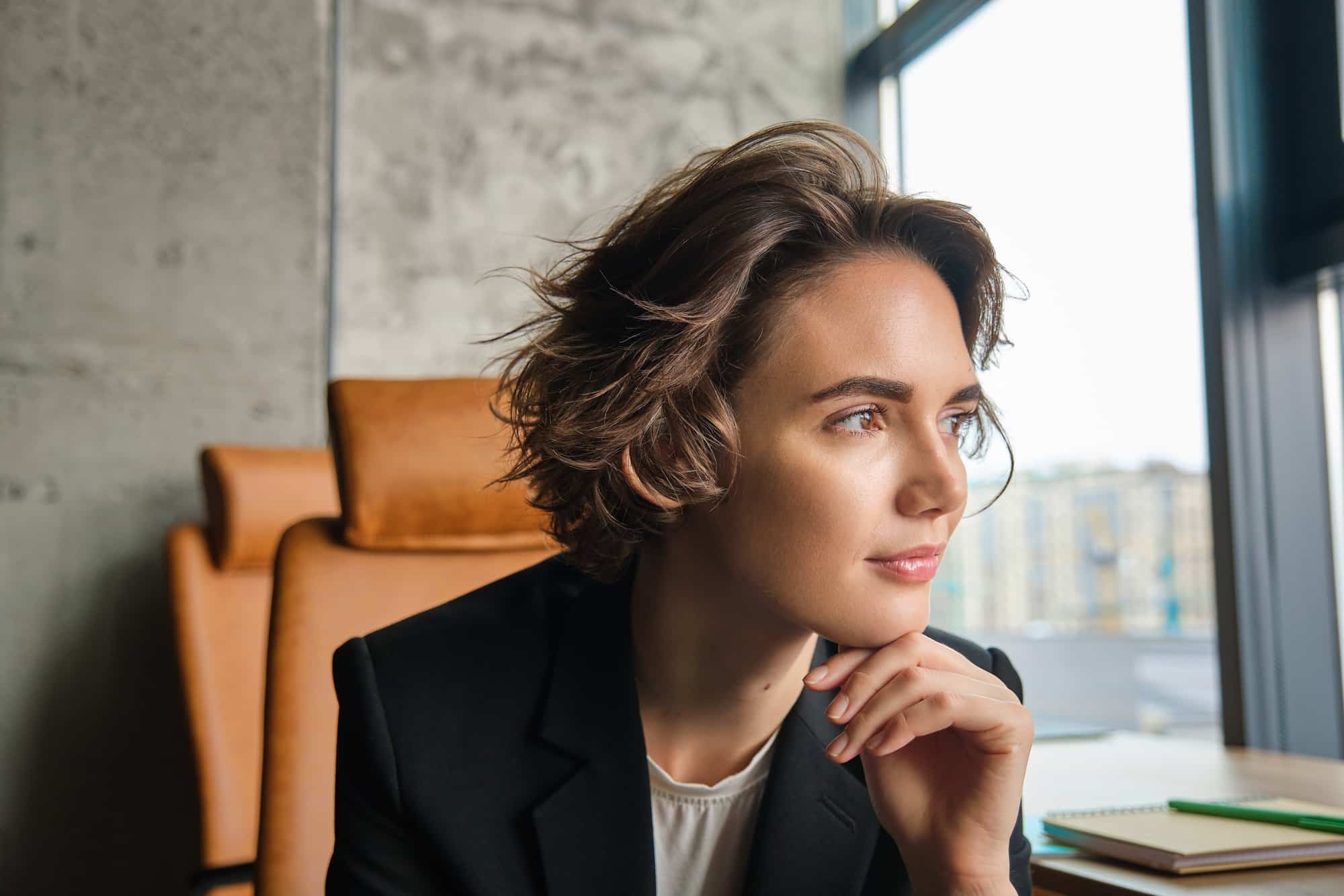Profile shot of confident businesswoman thinking, pondering and looking outside window, thinking of
